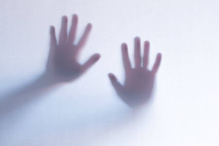 Blurred scary ghost hands behind a white glass background. Horizontal orientation
