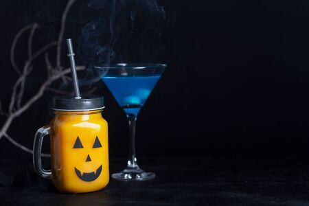 Halloween healthy pumpkin or carrot drinks in the glass jar, artificial eyeballs in a blue liquid on a black background with copy spaceの写真素材