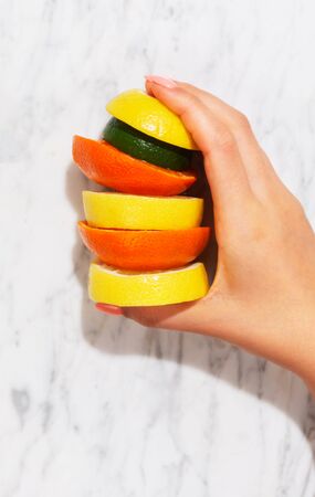 Citrus fruits. Orange, lemon, grapefruit, mandarin and lime on a trendy stone background. Top view, flat lay. Woman's hand grab or hold a pieceの写真素材