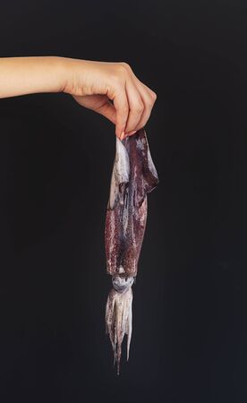 Female hand holds squid on a black background. This image may show dislike or describe of allergy conceptの写真素材