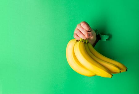 A woman holds bananas in her hand, inserted through a hole in torn green paperの写真素材