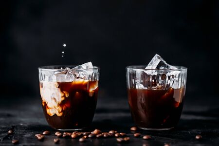 Coffee with ice in a glass, milk poured into a glass.
