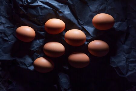 Getting ready for Easter. Eight brown eggs on dark background for coloring on crumpled, decorative paperの写真素材