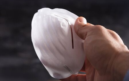 Man holds Anti coronavirus Covid-19 protective mask on dark background, horizontal