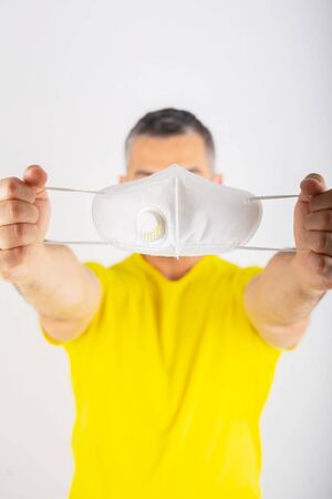 A man in yellow t-shirt holds medical mask. Coronavirus concept. Protect your health.の写真素材