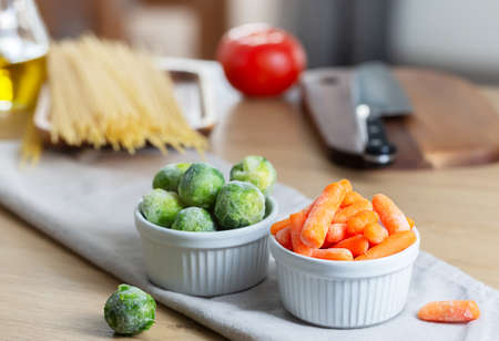 Frozen vegetables such as baby carrot and Brussels sprouts as well as dry pasta on the kitchen table. Freezing is a safe method to increase the shelf life of nutritious foodsの写真素材