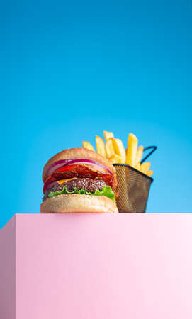 Fresh juicy beef hamburger and fried french fries placed on the pink stand and blue background. Copy space for text, trendy hero viewの写真素材