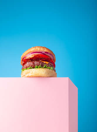 Fresh juicy beef hamburger placed on the pink stand and blue background. Copy space for text, trendy hero viewの写真素材