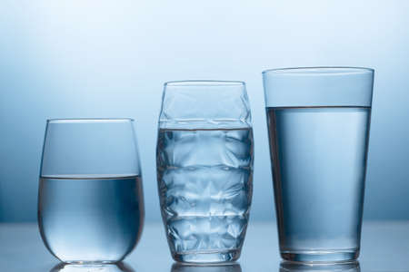 Fresh water in a three glasses on the blue background with reflectionの写真素材