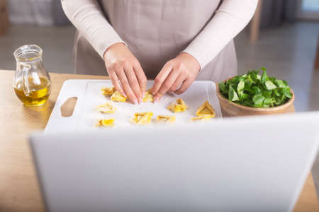 Woman preparing italian ravioli watching virtual culinary master class in a computerの写真素材