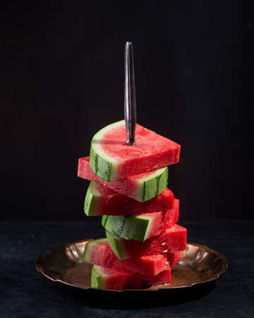 Red raw watermelon pieces on black background. It sweet, juicy flesh, usually deep red to pink, with many black seeds, although seedless varieties existの写真素材