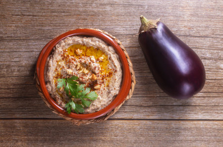 Levantine cuisine appetizer of baked eggplant and sesame paste with olive oil, spices, herbs and walnuts on a wooden background with eggplant. View from aboveの写真素材