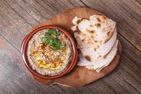 An appetizer Esme, baba ganush of Levantine cuisine made from baked eggplant and sesame paste, mashed with olive oil and spices, herbs and walnuts with lavash pieces on a wooden board. View from aboveの写真素材