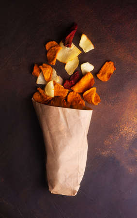 Vegetable chips made from potatoes, carrots and beets scattered from a kraft bagの写真素材