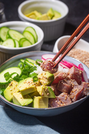 Someone holds piece of tuna fish over Poke Bowl, close up, selective focus