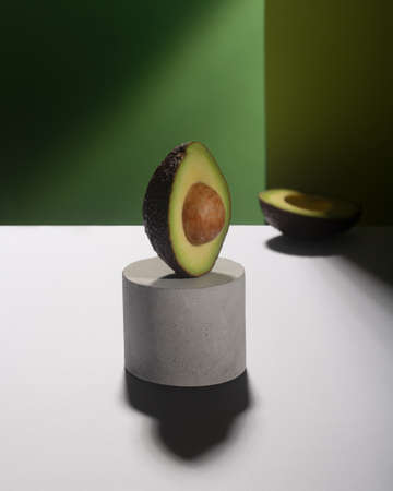Creative avocado balance on the concrete stand, green background, vertical