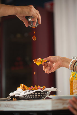 Man pouring spicy red tomato sauce on mexican snack nacho in a restaurant