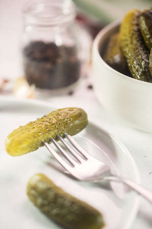 Pickled gherkin on a fork, salted cucumber on a white plateの写真素材