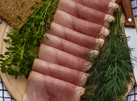 Delicious smoked ham on a wooden plate with fresh spicesの写真素材