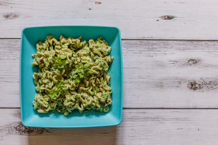 Whole grain pasta with spinach and basil on a blue plate on white wooden background, close upの写真素材