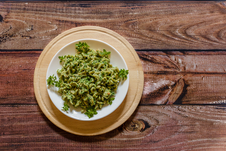 Whole grain pasta with spinach and basil on a white plate on  wooden background, close upの写真素材
