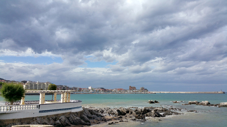view of the sea shore against the backdrop of the city center on a sunny day. Storm clouds in the sky. Castro-Urdiales, Cantabria, North Spain.の写真素材
