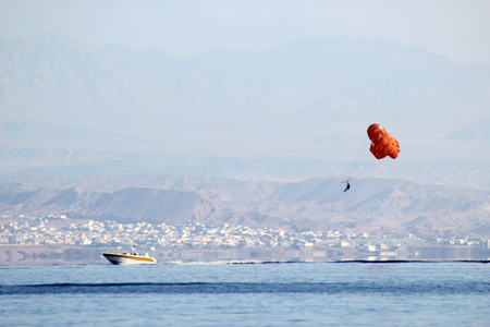 orange paraglider with a cheerful pattern hanging over a boat against a background of mountains in the hazeの写真素材