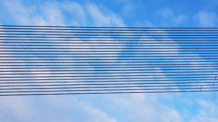 Black metal line rows against a blue sky with white clouds. Background of parallel lines arranged in...