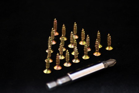 screws standing on hats in the shape of a triangle, and a nozzle for screwdriver on a black background.の写真素材