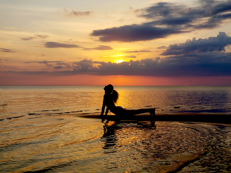 silhouette of a girl practicing yoga on the beach. Shooting against the sun. Sunset over the sea.の写真素材