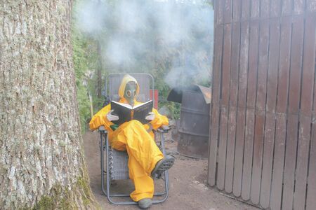 a human in a gas mask and in a yellow protective suit sits and reads a bookの写真素材