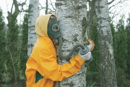 portrait of a man in a gas mask and a protective yellow suit hugs a birchの写真素材