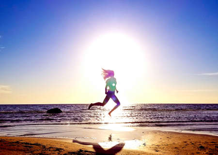 silhouette of a girl on the background of the sun disk in a jump on the sandy seashore in an interesting poseの写真素材