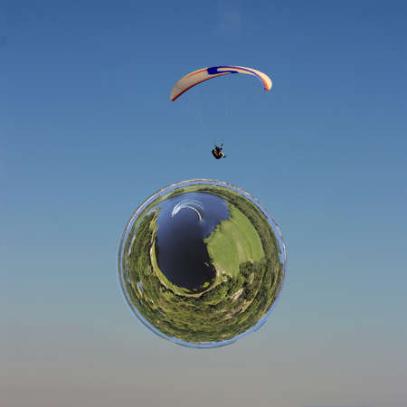 Little planet transformation of spherical panorama 360 degrees. Spherical abstract aerial view on a man is flying on white paraglider in the sky above from a curved space.の写真素材