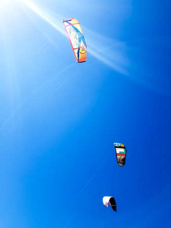 three sails from kitesurfing against a blue sky with sun beamsの写真素材