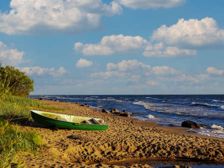 on the sandy shore of the sea lies a small wooden boat. Cloudy warm summer day on the Batian Sea.の写真素材