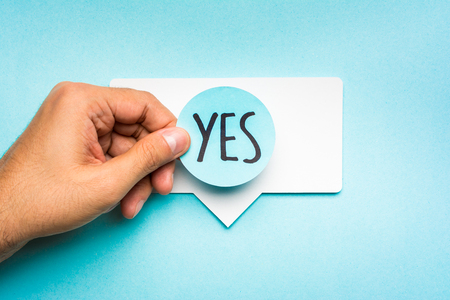 Yes banner concept. Hand showing speech bubble with text yes and blue backgroundの写真素材