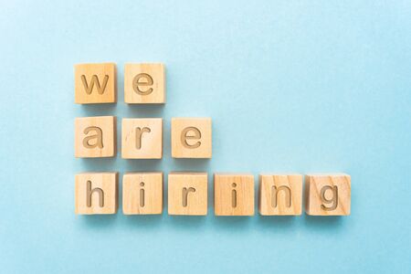 Close up of "We are hiring" on small wood cubes in the middle of paper with blue background. Recruiting and Employment concept.の写真素材