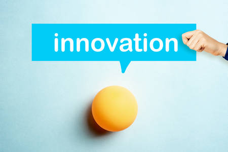 Concept of Innovation with a hand showing a speech bubble and yellow table tennis ball on blue backgroundの写真素材