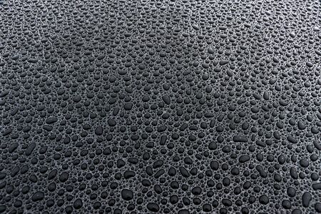 beaded water droplets on black surfaceの写真素材