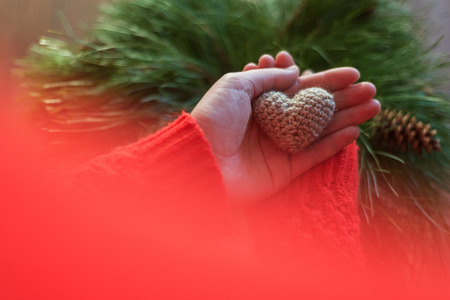 Woman in red jacket holding a small knitting heart on wooden background. Love and the concept of Valentines Day.の写真素材
