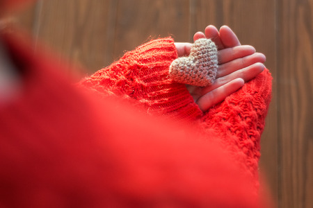 Woman in red jacket holding a small knitting heart on wooden background. Love and the concept of Valentines Day.の写真素材