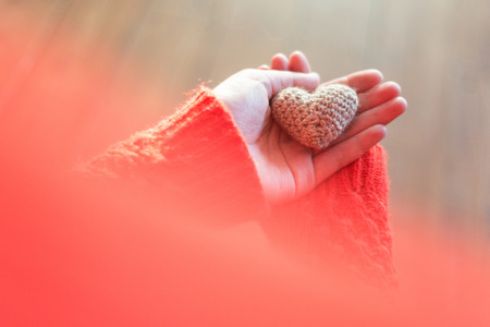 Woman in red jacket holding a small knitting heart on wooden background. Love and the concept of Valentines Day.の写真素材