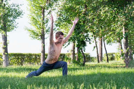 A young, beautiful white man in sports clothes is doing a stretch in the Park on the green grass. Prepare a warm-up for yoga or fitness classes. violation of isolation modeの写真素材