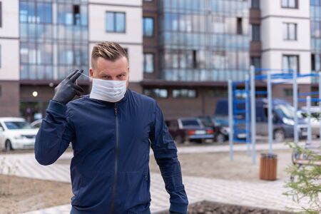 Concept of kovid 19. portrait of a Caucasian man on the street in the city. wearing a medical mask and gloves to prevent the rapid spread of the corona virus.keeping a safe distanceの写真素材