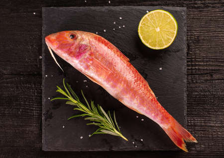 Raw barbun with lime and rosmary on black wooden plank. Top view.