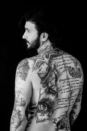Tattooed naked man with messy hair showing his back on black backgroundの写真素材