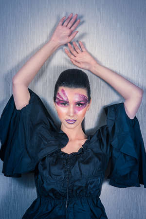 Beautiful Caucasian woman with purple face painting and crystals on her face raising hands, on a...