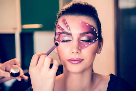 After painting model's face with purple and crystals, the make-up artist is applying the powder on...