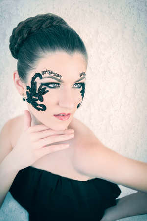 Young female model with braided blonde hair, big green eyes and decorative black lace on her face, touching her chin, on white lace backgroundの写真素材